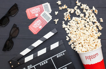 minimalistic, stylish flat lay. Movie time,  Cinema minimal concept. Movie clapperboard, 3d glasses, movie tickets and popcorn on a black wooden background.