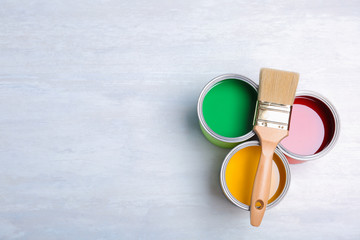 Cans with paint and brush on light background, top view. Space for text