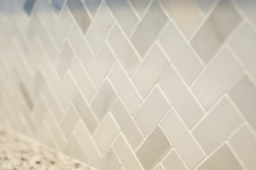 Close detail of a new small tile herringbone pattern professionally installed in a home kitchen.  Warm grey tones.  Horizontal image with shallow depth of field.