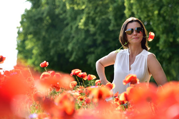 A woman standing on a poppy field, holding a poppy flower in her mouth.