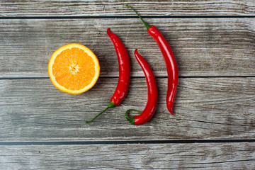 Flat-lay red chili pepper and cut in half an orange on a gray background