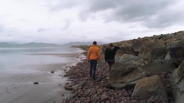 Two friends walk along a pebbly beach at the Irish west coast