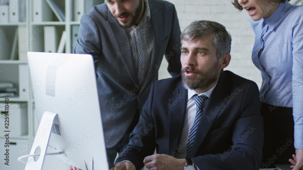 Poster tilt up shot of three entrepreneurs working together in office and viewing something on desktop comp