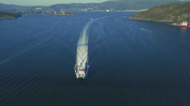 Aerial tracking shot of very fast passenger ferry passing the suspension bridge. Weather is sunny and there are cars crossing the bridge.