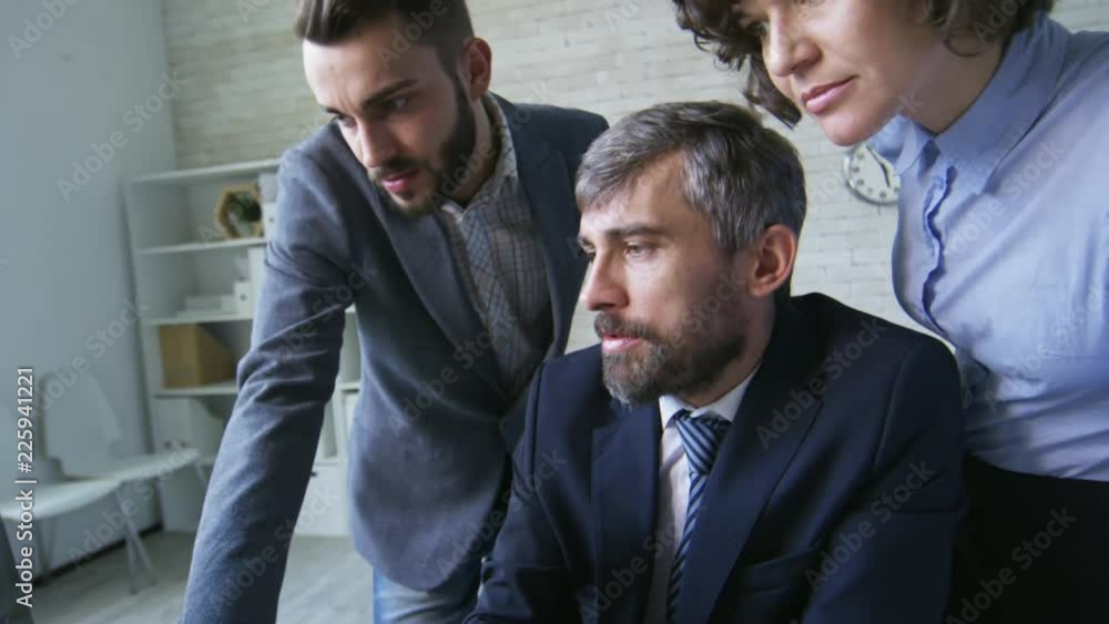 Poster medium shot of three colleagues in formal clothes using laptop computer in office to see work result