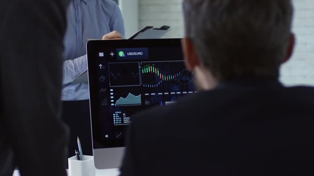 Three businesspeople using statistics and computer software to see and analyze currency exchange rates and make financial decisions