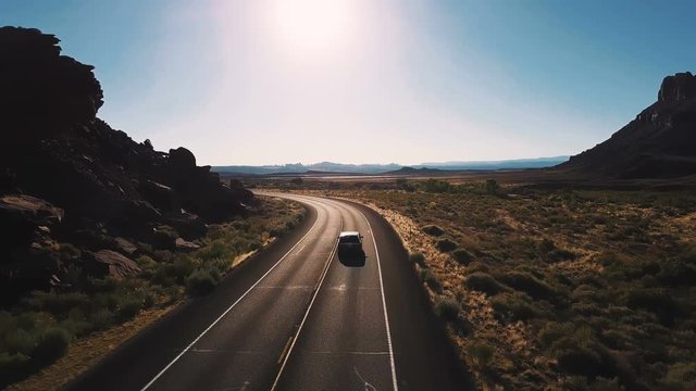 Drone camera follows minivan car turning left on desert highway road between breathtaking open spaces and mountains.