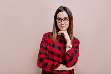 Pretty smart female dressed shirt and glasses, looking with satisfaction at camera, being happy. Studio shot of good-looking attractive woman isolated against blank studio wall.