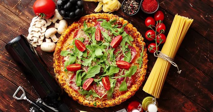 Italian food background with pizza, raw pasta, spices, herbs, wine, and vegetables on wooden table. Top view.