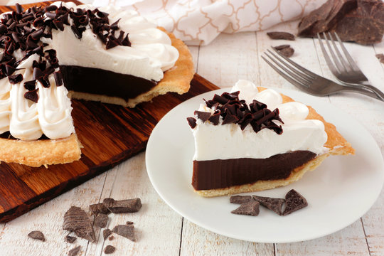 Slice of sweet chocolate cream pie. Close up table scene with a white wood background.