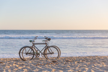 Two bikes on beach against ocean waves