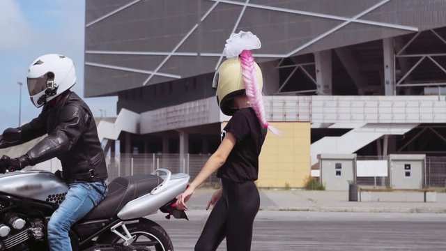 Fabulous young Caucasian woman in helmet and pink braid sitting on motorcycle. Likable young man and girlfriend riding bike.