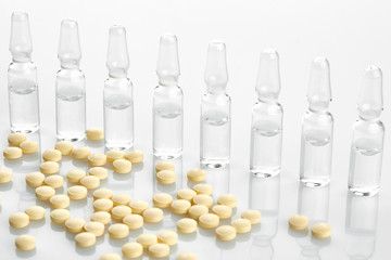 Ampoules with medicine and yellow tablets on white background