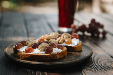 Delicious homemade healthy snack crostini with grapes, walnuts and ricotta on wooden table, close up
