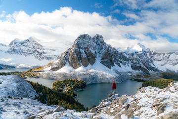 A lone man in a red jacket watches a cloud covered peak