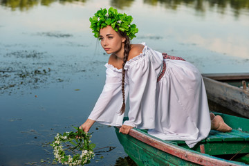 Young sexy woman on boat at sunset. The girl has a flower wreath on her head, relaxing and sailing on river. Fantasy art photography.