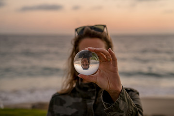 Girl holding a lens ball on the beach at sunset time