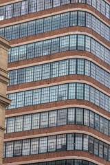 A tall building with many window. The viewer is looking at the corn of the building. A red brick facade is below the windows. A white brick facade is above the windows. This is a vertical picture.