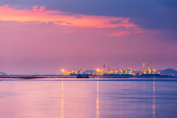 Logistics and transportation of Container Cargo with working crane bridge in shipyard. Cargo shipping and commercial terminal in seaport at sunset. Industrial landscape with gantry cranes in sea port.