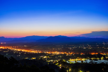 Fototapeta premium Aerial view at Doi Khao Kwai during blue zone after sunset. Mountain range as background with light tail on main road at Chiangrai city and big pond as foreground