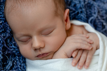 Newborn - baby, face close-up. The sleeping Newborn boy under a white knitted blanket lies on the blue fur.