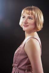 Optimistic Smiling Caucasian Blond Female in Pink Dress. Posing Against Black Background. Looking...
