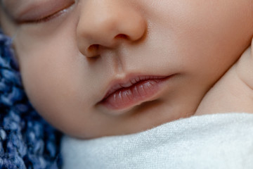 Newborn - baby, face close-up. The sleeping Newborn boy under a white knitted blanket lies on the blue fur.