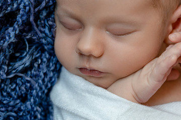 Newborn - baby, face close-up. The sleeping Newborn boy under a white knitted blanket lies on the blue fur.