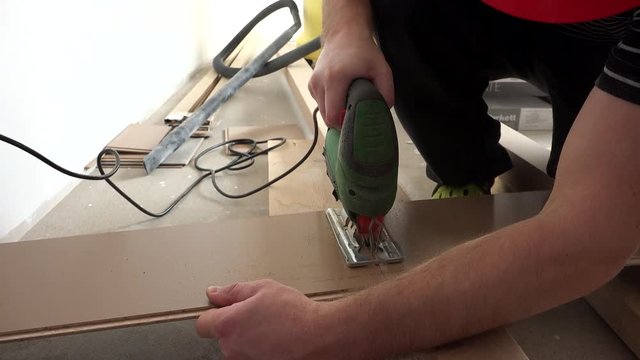 Male worker hands cutting flooring laminate board with jigsaw