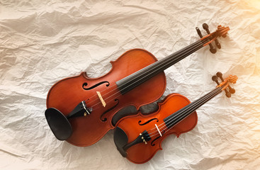 Fototapeta na wymiar Two different size of violins put on background,warm light tone,blurry light around