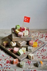 various national Oriental sweets, with paper flags of Turkey, Turkish delight on a wooden white brushed stand and on a white brushed background, vertical, the concept of the independence day of Turkey