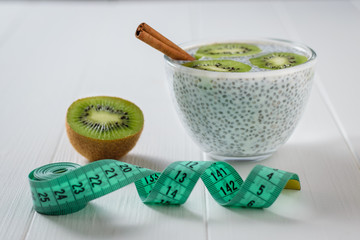 Cinnamon sticks, kiwi fruit and a glass bowl of Chia seeds with milk and measuring tape on the white table.