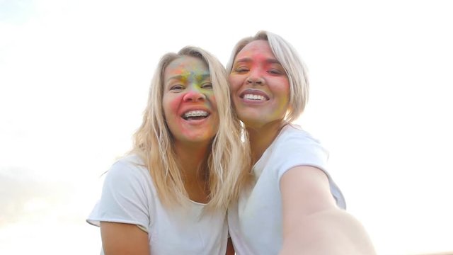 Friendship concept. Girlfriends make selfie in paints of holi