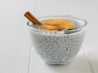 Chia seed pudding with slices peach on a white wooden table.