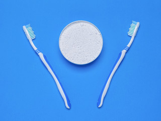 Two toothbrushes and a jar of tooth powder on the blue table. The view from the top. Flat lay.