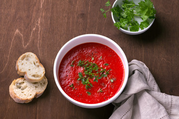 Delicious vegan soup of baked tomatoes and sweet peppers with herbs in a white plate on a wooden background, top view, horizontal