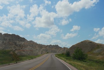 Fototapeta premium Paved road winding around the dramatic landscapes and rock formations at Badlands National Park in South Dakota, USA.