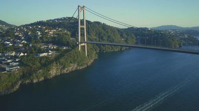 Wide shot of suspension bridge with pillar and landscape. Weather is sunny and there are cars crossing the bridge.