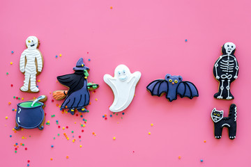 Fresh halloween gingerbread. Icing cookies in shape of halloween evils like black cat, skeleton, bat, ghost, witch on pink background top view copy space