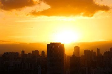 Fototapeta premium Pôr do sol com avião passando ao fundo, sobre os prédios de uma metrópole
