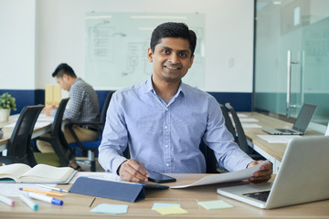 Smiling handsome Indian developer working at table in open space office