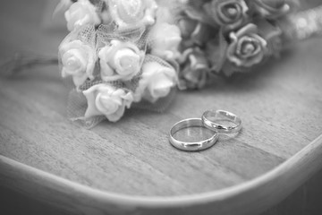 Wedding rings on the table against the background of bouquets of roses close-up. Black and white image.