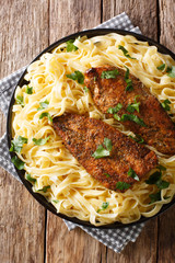 American fried chicken breast lazone with fettuccine pasta in a creamy sauce closeup on a plate. Vertical top view