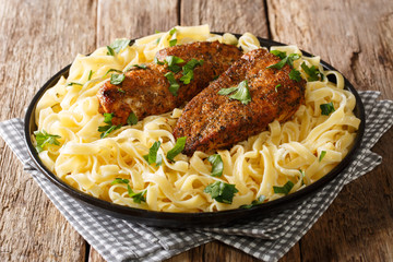 Fried spicy chicken breast served with fettuccine pasta and cream sauce close-up on a plate on the table. horizontal