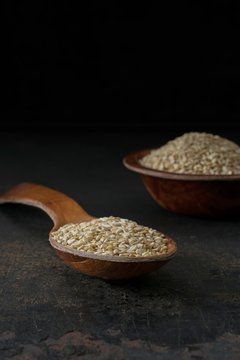 A low light image of a wooden spoon and bowl of sesame seeds with copy space for your text