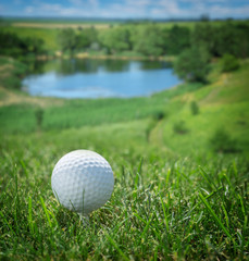 Golf ball on course. Beautiful green landscape and lake at the background.
