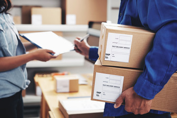 Courier with parcels signing document in delivery service office