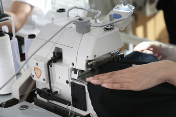 tailors hand on the black fabric in sewing machine