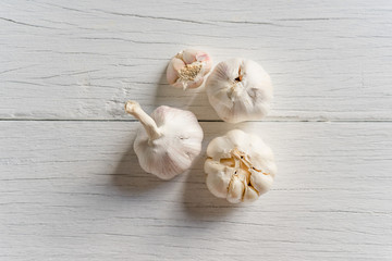 Organic garlic whole and cloves on white wood background.