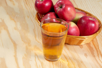 Glass of apple juice in front of a basket full of red ripe apples